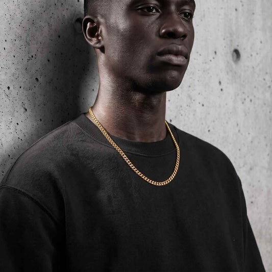 Close-up portrait of a male model wearing the iceX 7mm gold Miami Cuban chain over a black sweatshirt against a textured concrete wall.