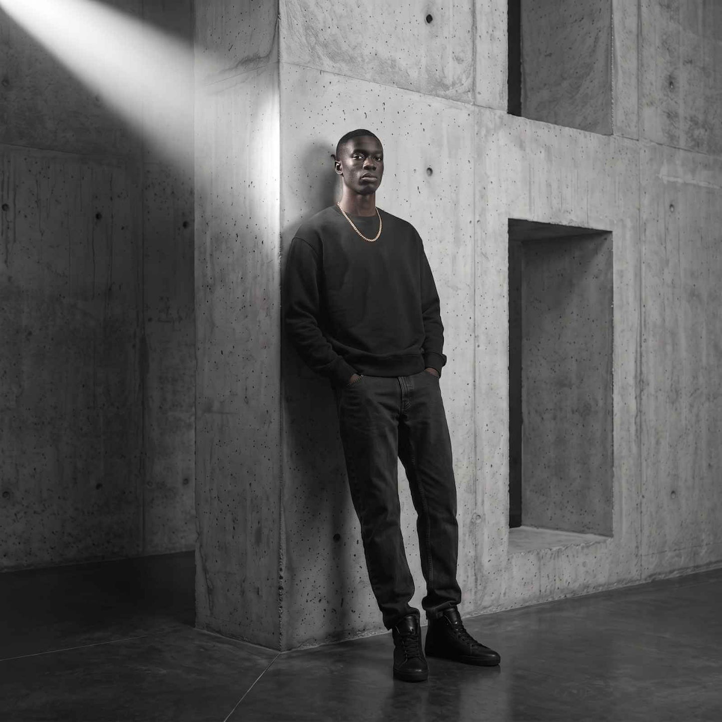 Full-body shot of a male model wearing the iceX 7mm gold Miami Cuban chain with a black sweatshirt and jeans under a dramatic shaft of light.